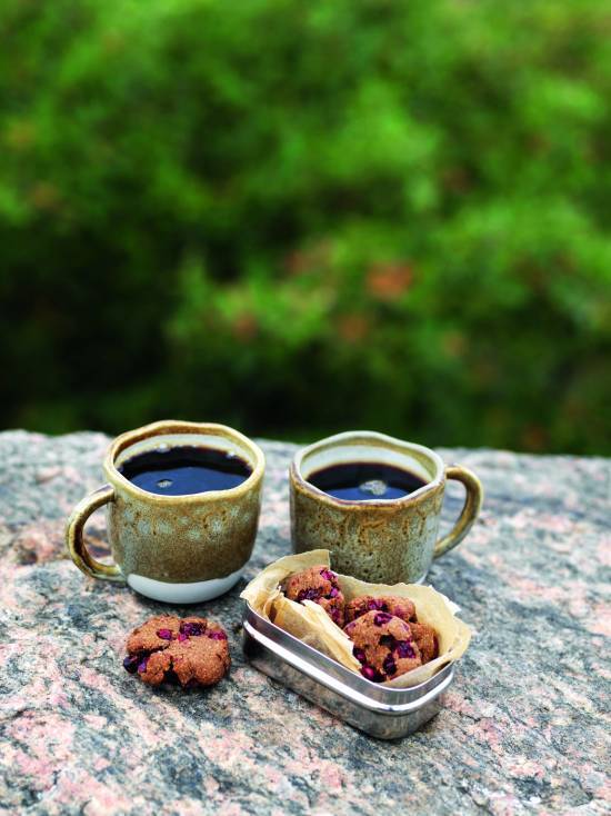 två tahinicookies på en sten med två kaffekoppar bakom