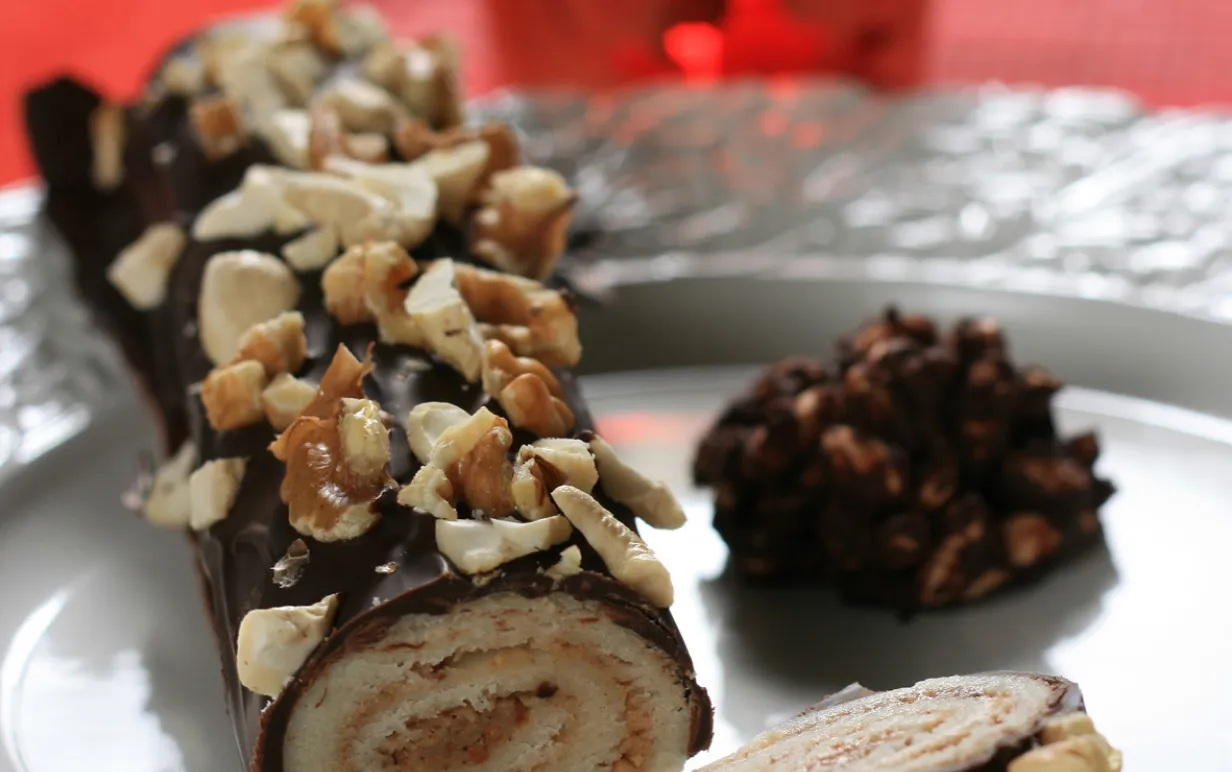 Marsipan- och nougatrulle, dekorerad med cashewnötter och valnötter, på ett fat.