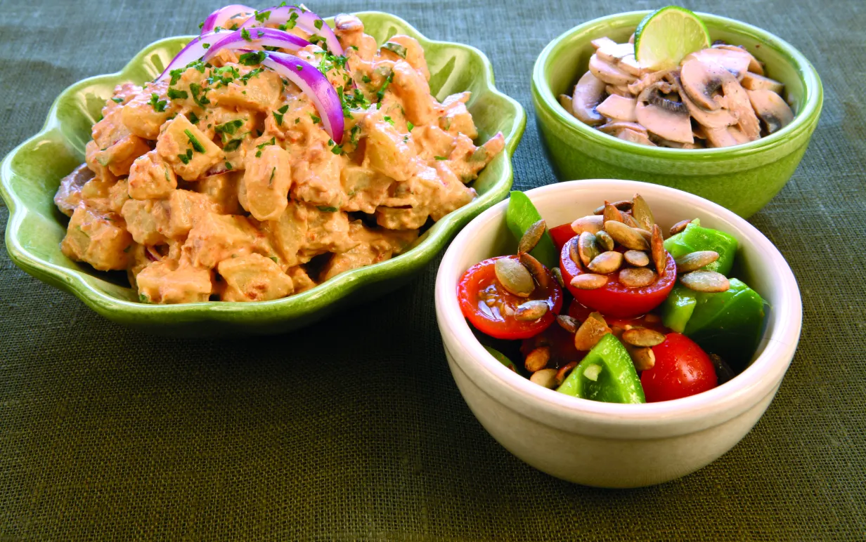 Tre skålar, en med potatissallad, en med råa champinjoner och en med tomat och paprika.