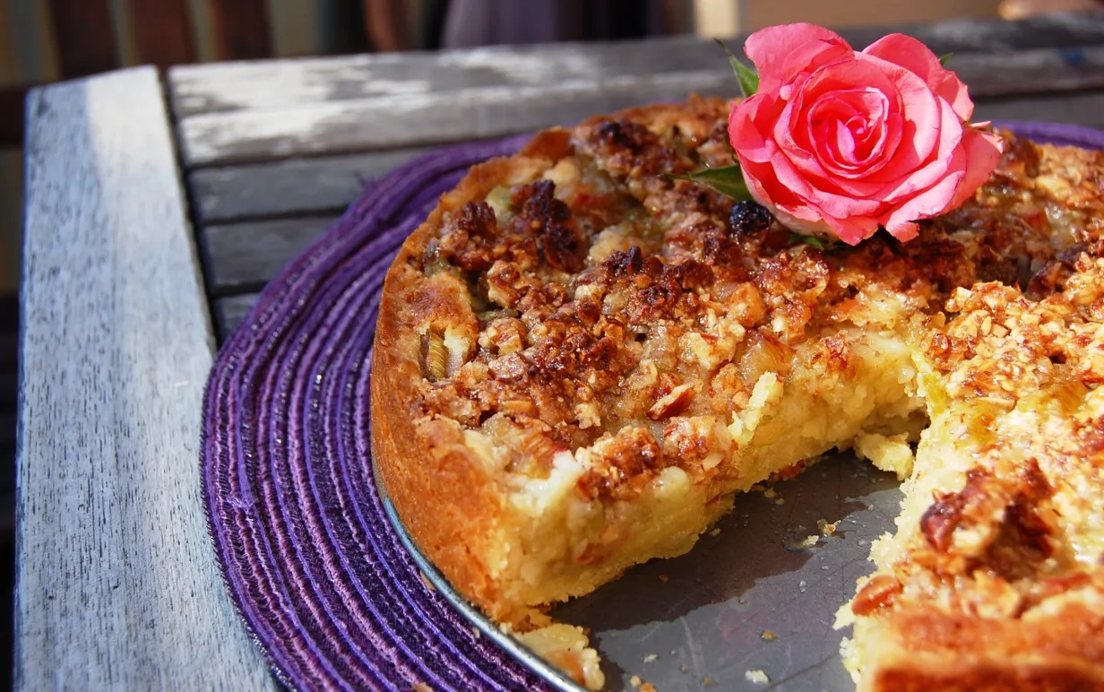 Rabarbertårta dekorerad med en rosa ros, på en lila duk.