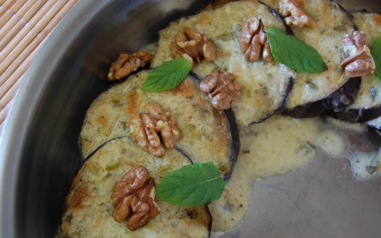 Ostkrämsgratinerade auberginer i en grå form, dekorerade med mynta och valnötter