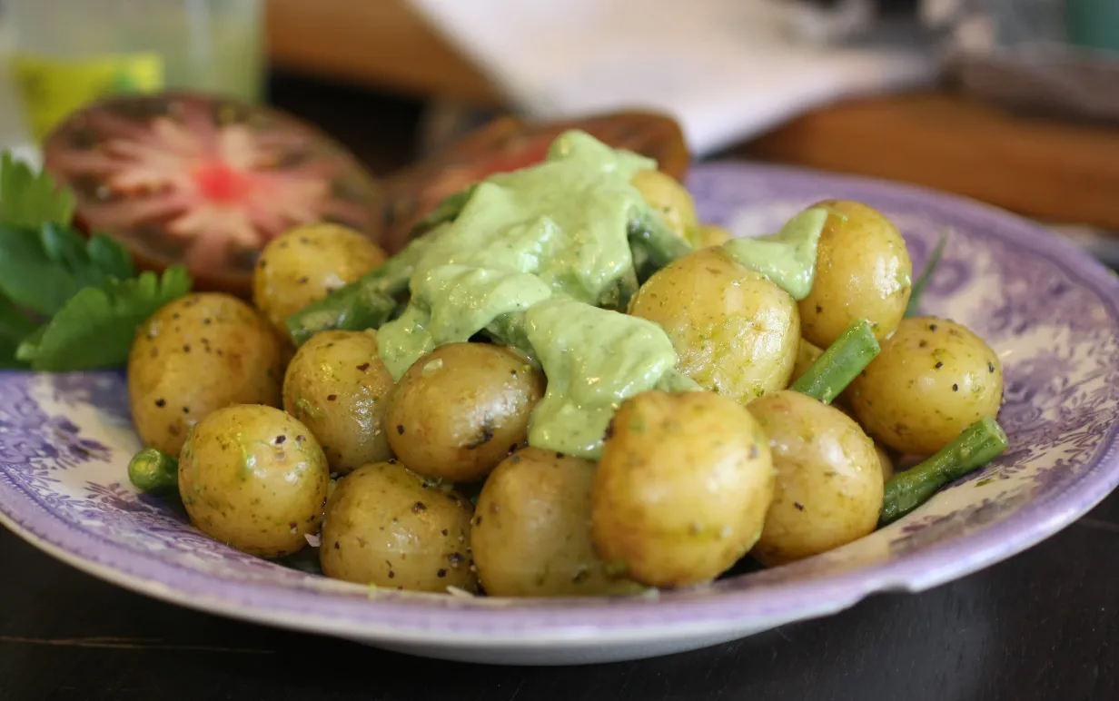 Potatissallad med grön dressing och haricoverts på ett blåvitt fat.