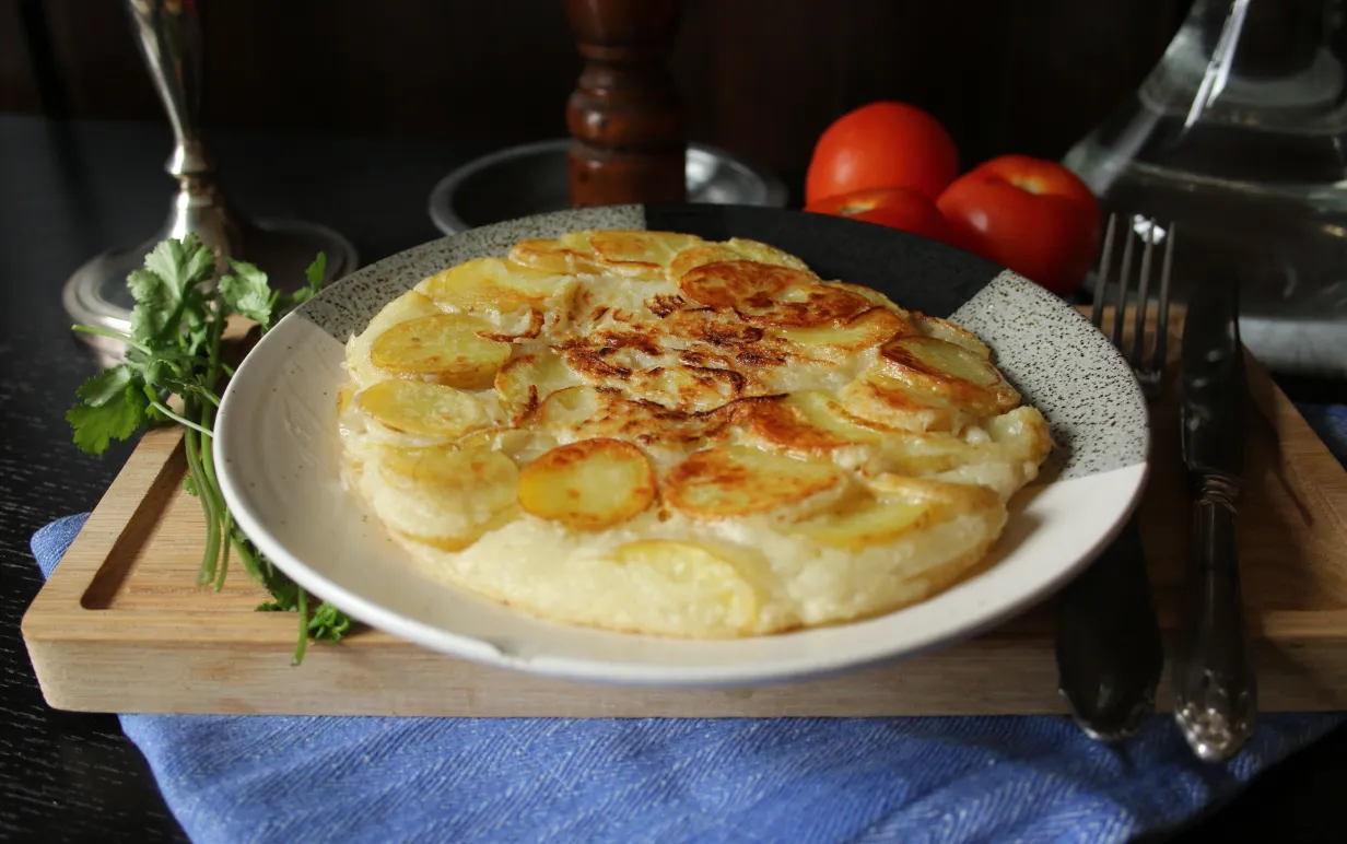 en vit tallrik med spansk potatisomelett på en skärbräda, bredvid tallriken ligger några tomater