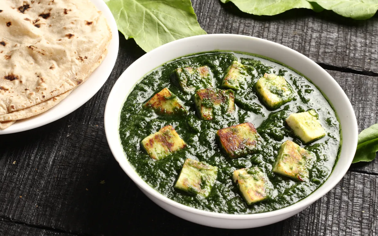 Palak paneer och naan bröd på ett mörkt bord