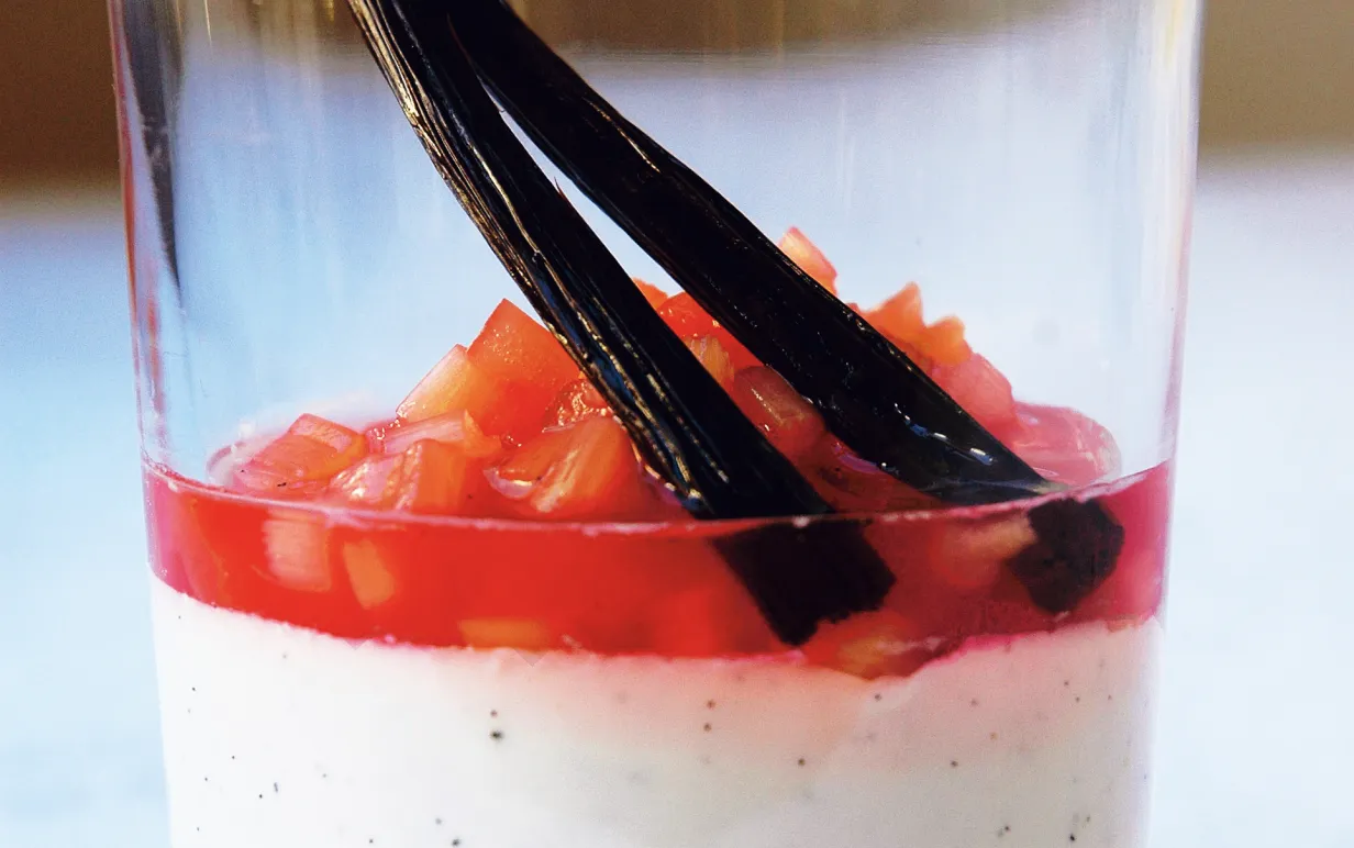 Pannacotta med kokosmjölk och rabarberkompott i ett glas, dekorerad med vaniljstång.