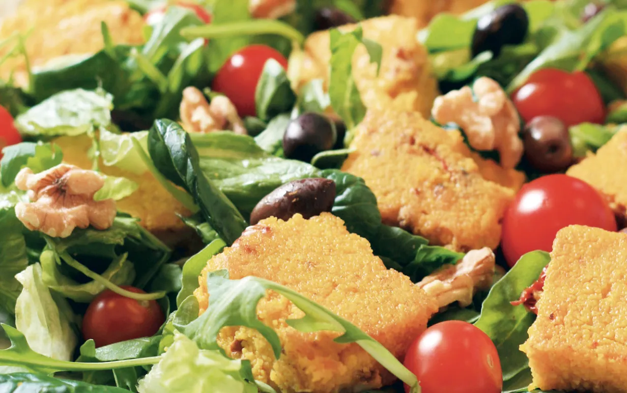 Saffranspolenta med körsbärstomater, oliver, sallad och valnötter på en tallrik