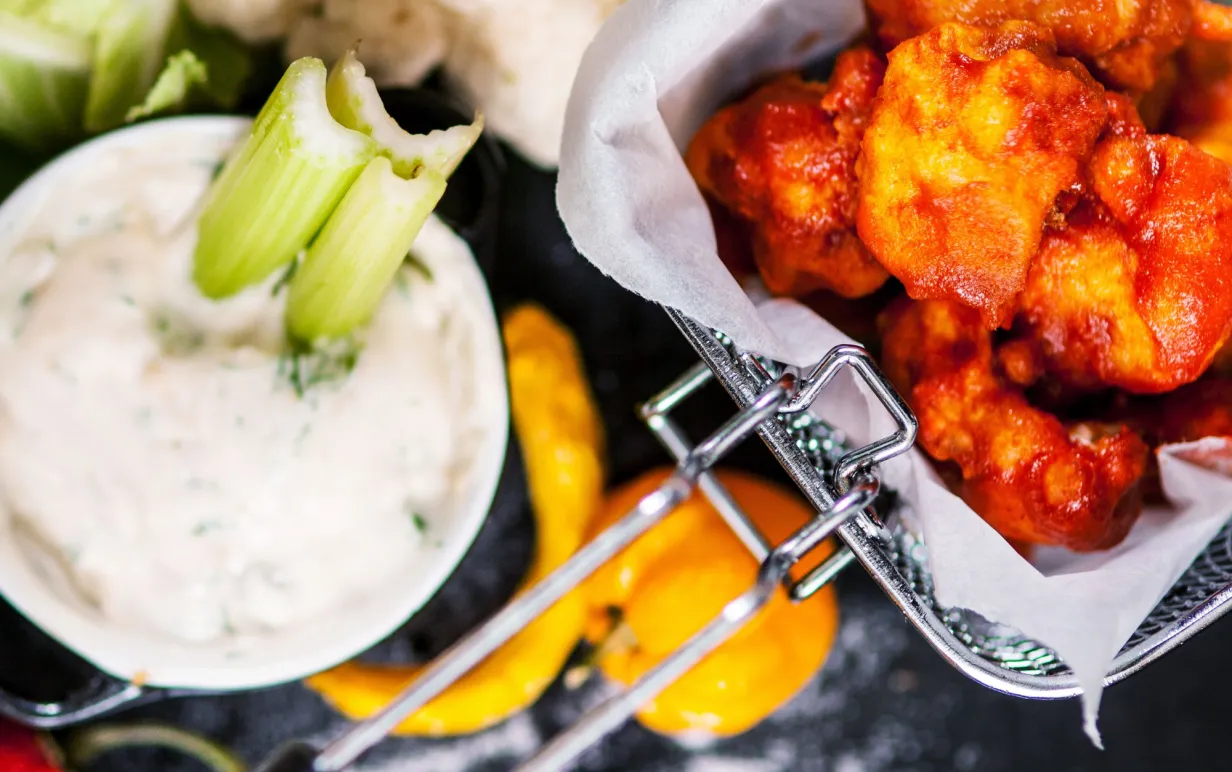 Buffalo wings av blomkål i en frityrkorg, bredvid står en skål med blåmögelostsås