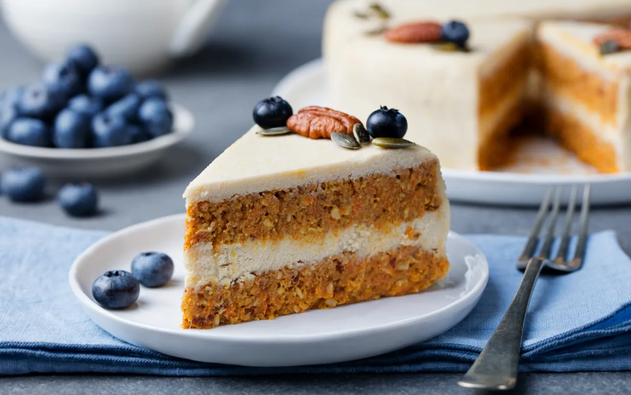 Vegansk morotskaka på en vit tallrik, bredvid tallrik ligger några blåbär