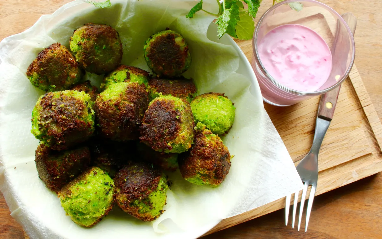 ärtbollar i en vit skål på en skärbräda, bredvid står en skål med rödbetssås