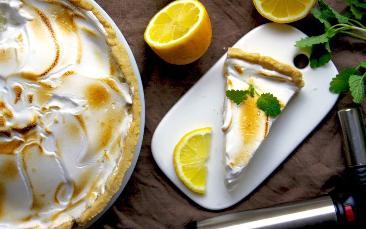En citronpaj med marängtäcke, bredvid pajen ligger några delade citroner