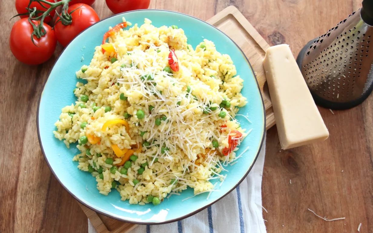 Svamprisotto på en blå tallrik på ett träbord, bredvid tallriken ligger några tomater