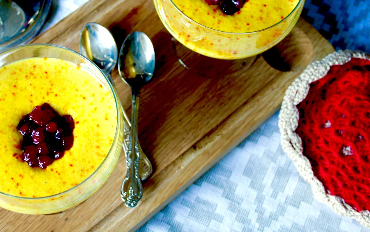 Två bägare med mannagrynsgröt med smak av saffran, toppade med lingonsylt, på en träskärbräda.
