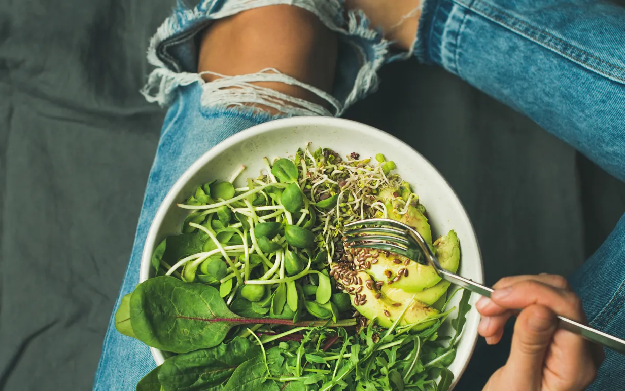 Skål med groddar, avokado och spenat på en persons ben
