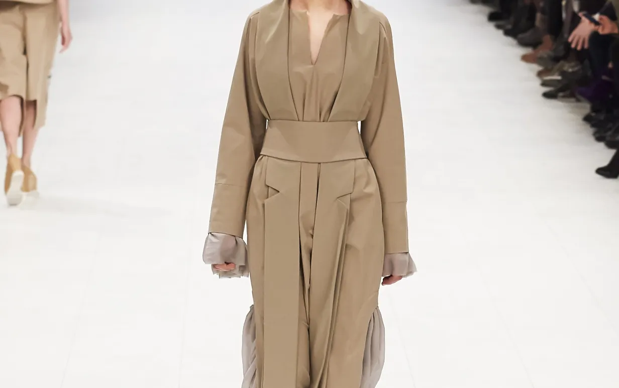 En catwalk med en person i mitten med en trenchcoat och åskådare på varje sida