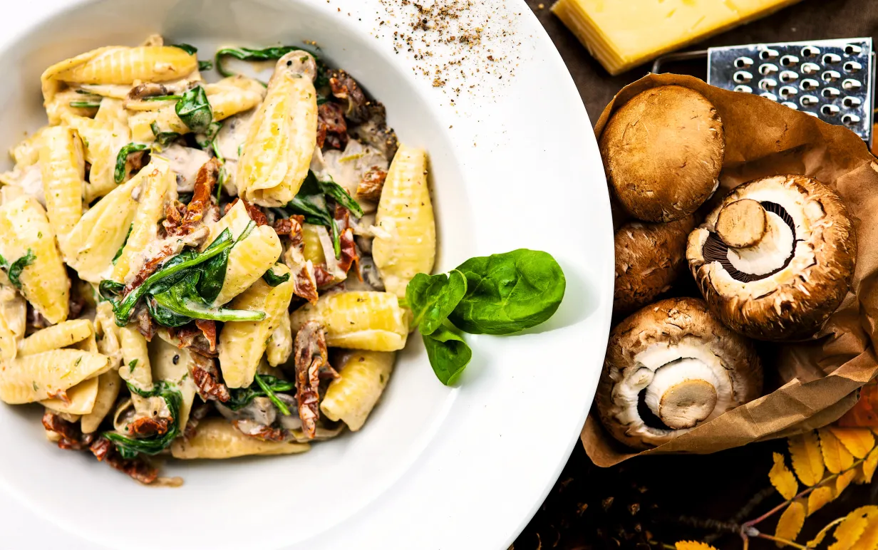 Gräddig pasta på vit tallrik, det ligger champinjoner intill tallriken