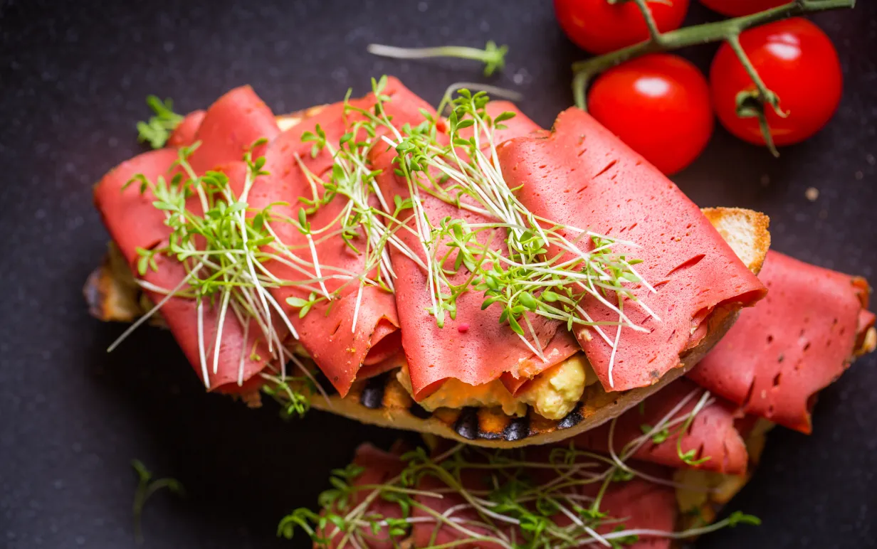 Vegansk skinka på en macka toppad med en gröna blad