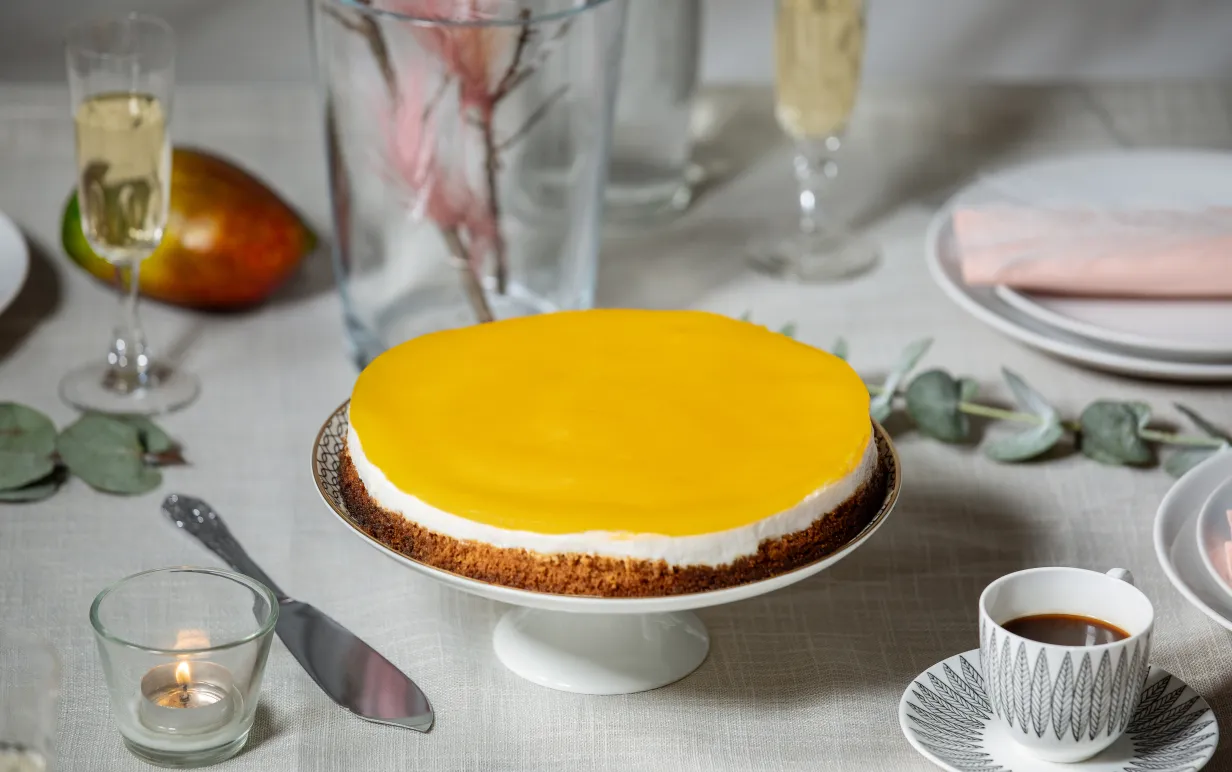 Vegansk cheesecake med mangoglasyr på ett tårtfat.
