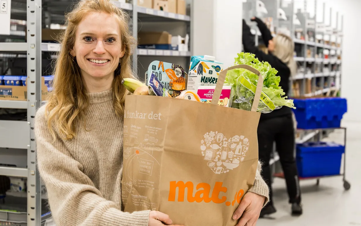 Person står i en lagerlokal med en matkasse fylld med veganska produkter