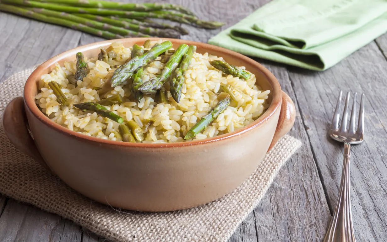 Skål med risotto toppad med sparris på ett bord