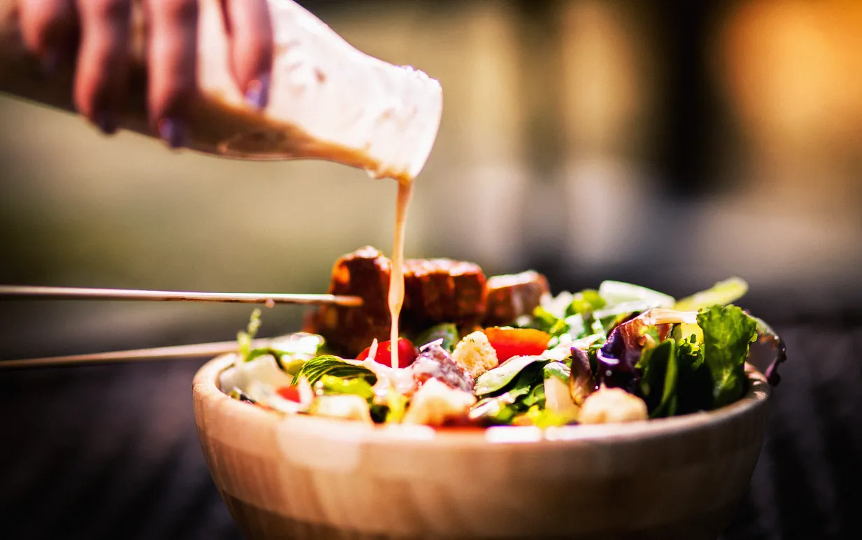 Vegansk caesarsallad med tempeh och en hand som häller på dressing