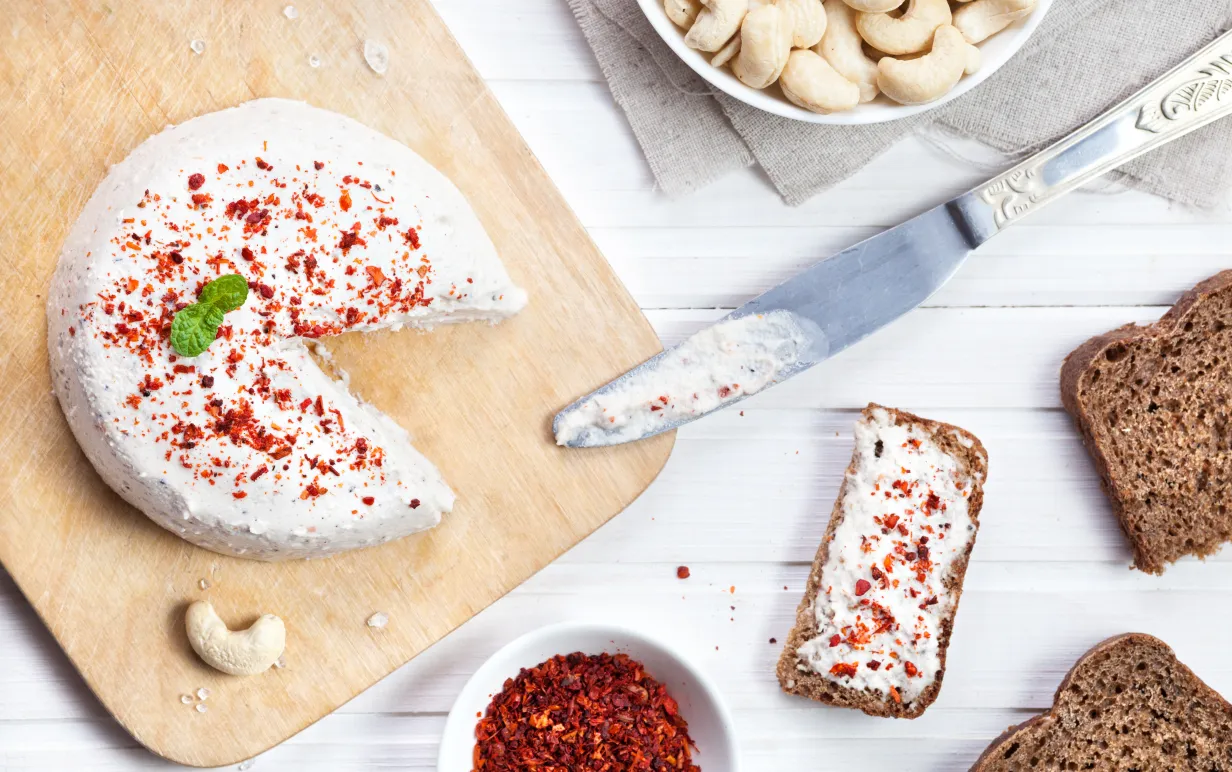 Vegansk cashewost toppad med chiliflingor på en skärbräda.