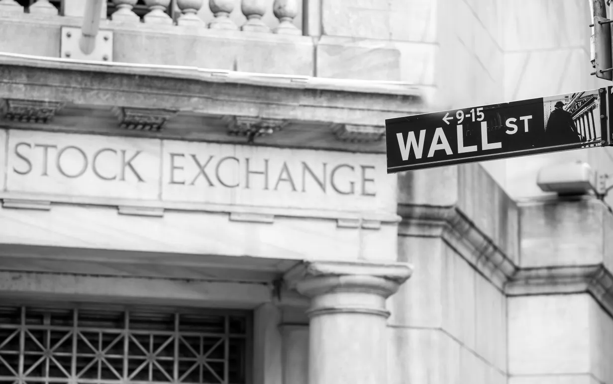 Bild på vägskylt med texten "wall st" framför en mur med texten "Stock exchange"