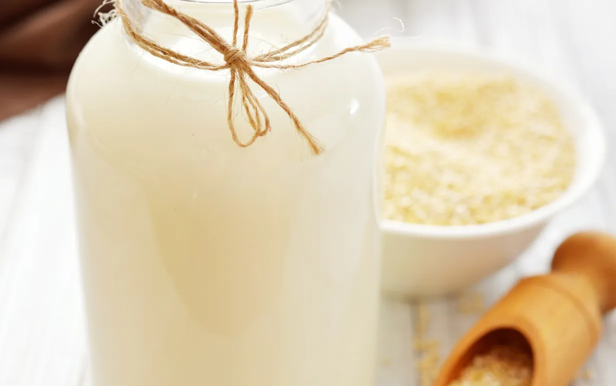 Växtdryck av quinoa i en glasflaska med vit quinoa på ett bord