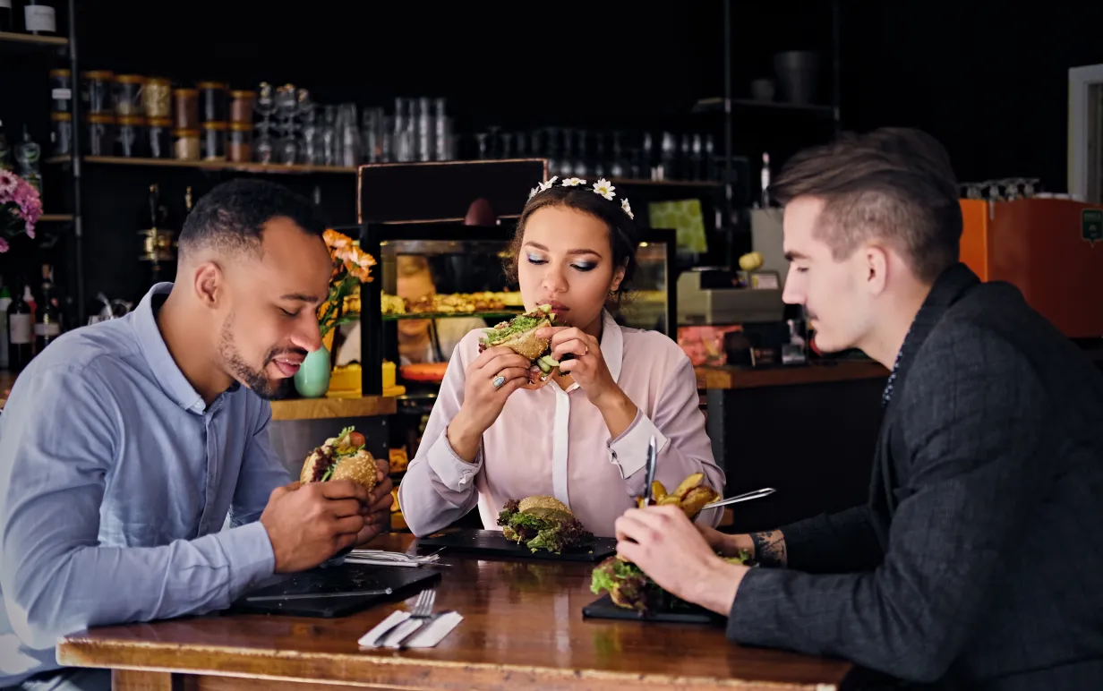 Tre personer sitter och äter på veganska mackor på en pub