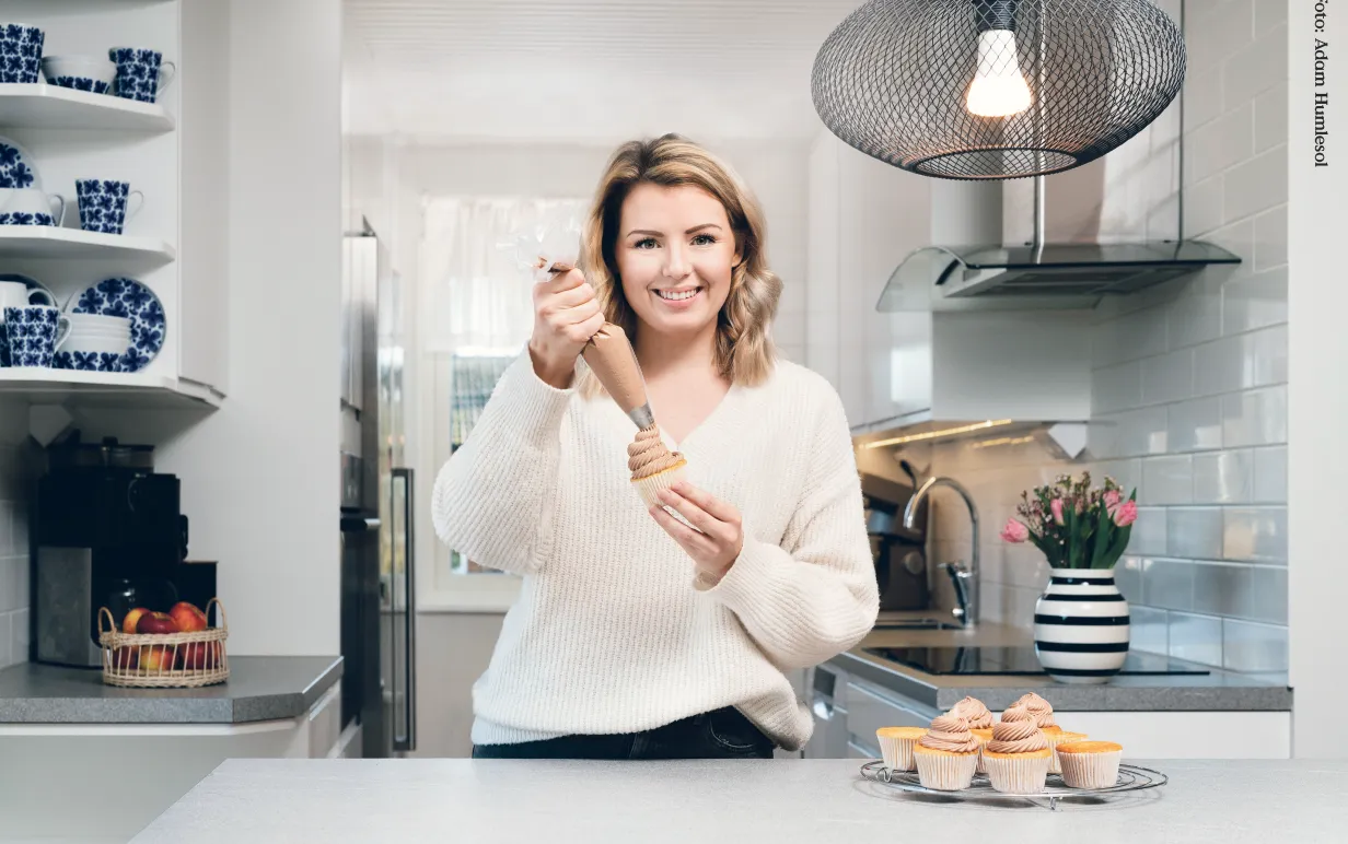 Frida Svanberg står i sitt kök och spritsar muffins