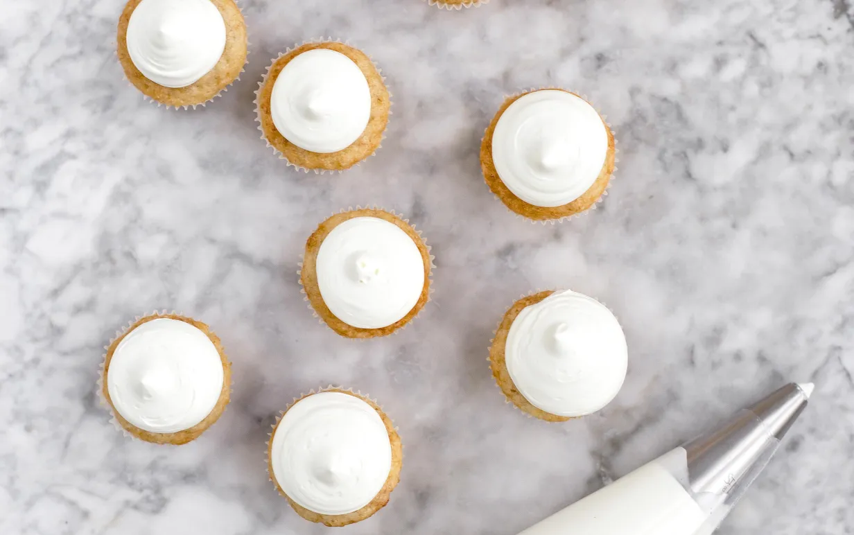 Bananmuffins med aquafaba har här gräddats i minimuffinsformar i 175°C i 13-15 minuter. Godisfluff av smälta bananskumgodisar är spritsat med en rund spritstyll på en centimeter.