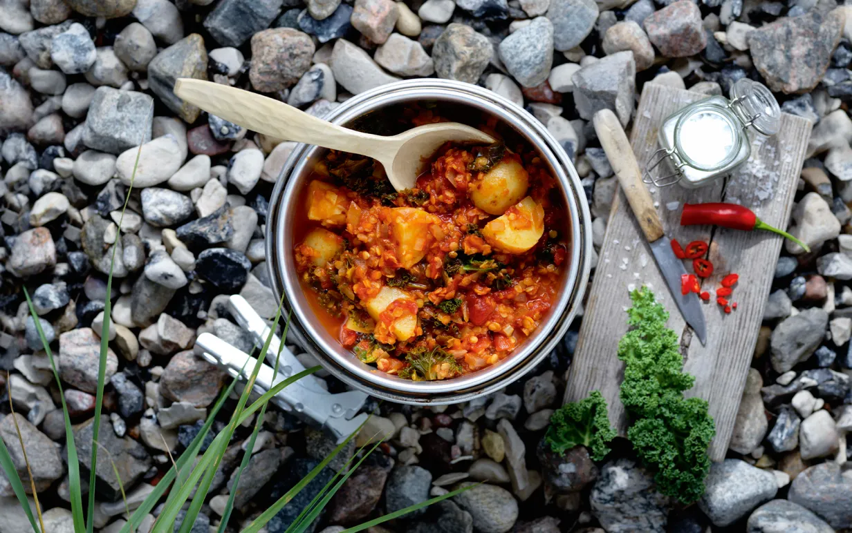 Potatis one pot i en gryta på småstenar med en träbräda med en kniv, röd chili och flingsalt bredvid