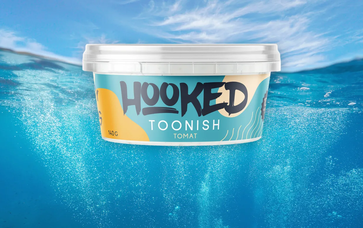 Plastburk med "Toonish" i smaken tomat mot bakgrundsfoto föreställande himmel och hab, taget delvis under vattenytan.