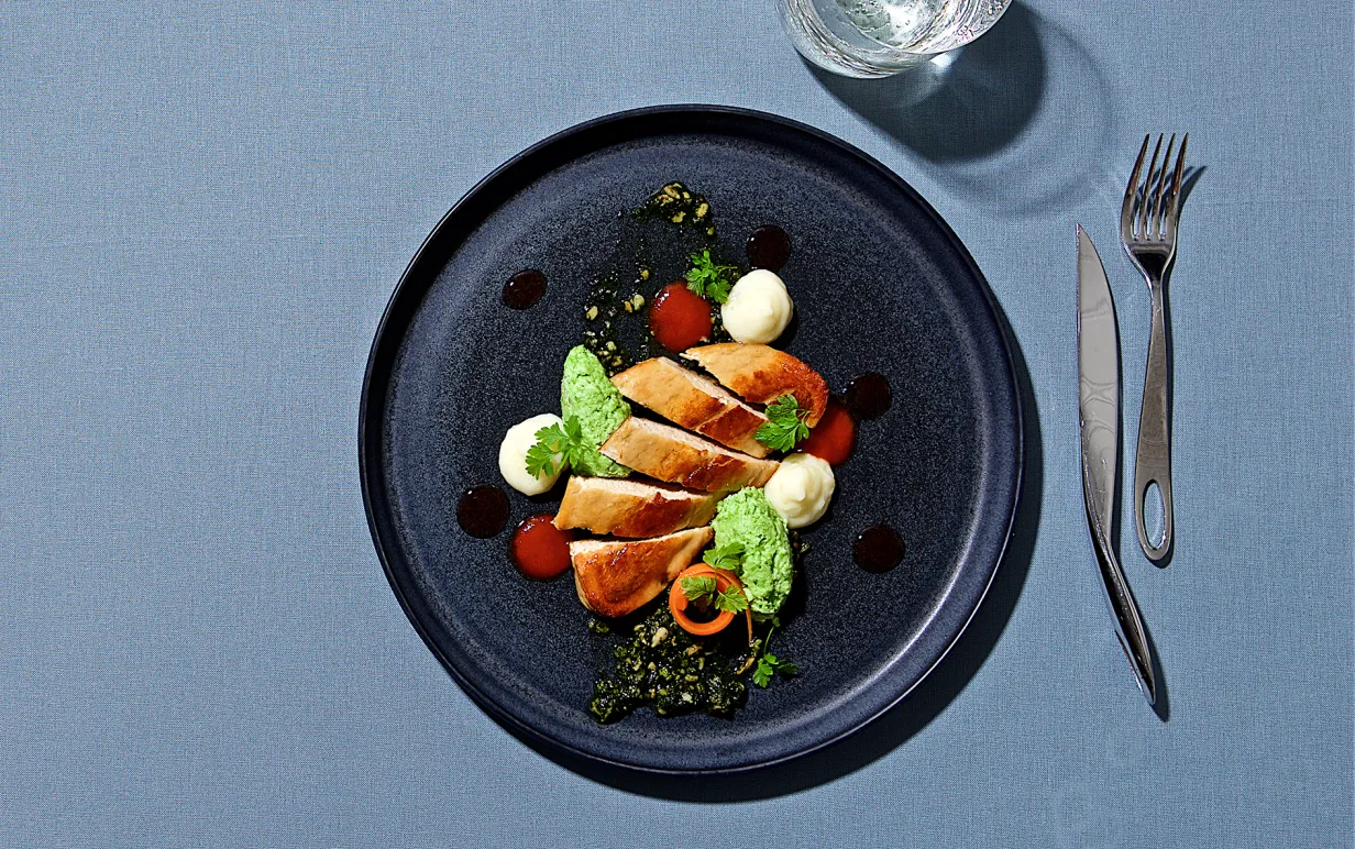 Vegansk quornfilé på tallrik med bestick och vattenglas runtom, fotat ovanifrån mot blå bakgrund.