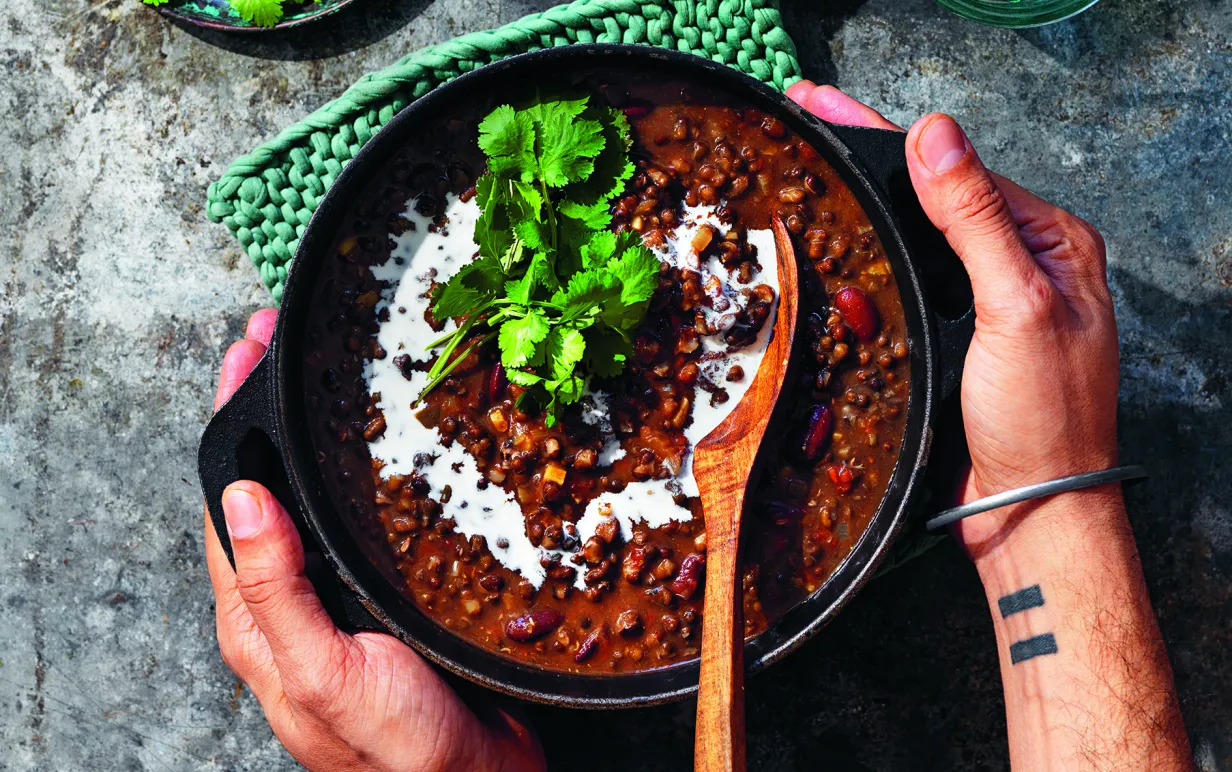Dal makhani i gryta på bord. Två händer håller om grytan.