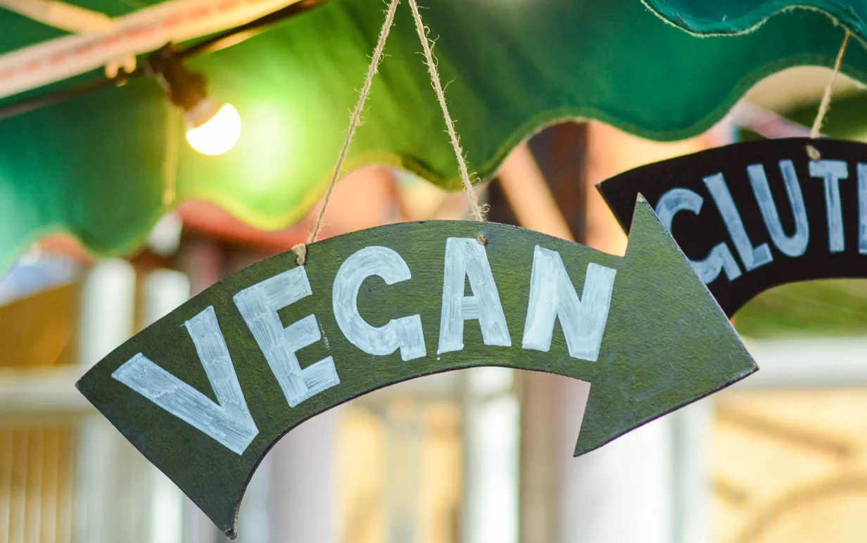 Pilformad skylt med texten "vegan", hängandes från ett parasol i dovt upplyst miljö.