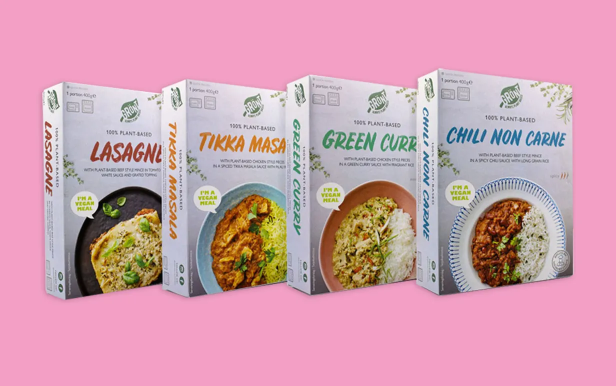 Grönts fyra nua veganska färdigrätter, uppradade bredvid varandra i förpackning, mot rosa bakgrund