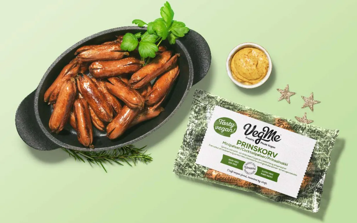 Prinskorv från VegMe i gjutjärnsgryta mot grönbakgrund, med förpackning och en liten skål senap bredvid.