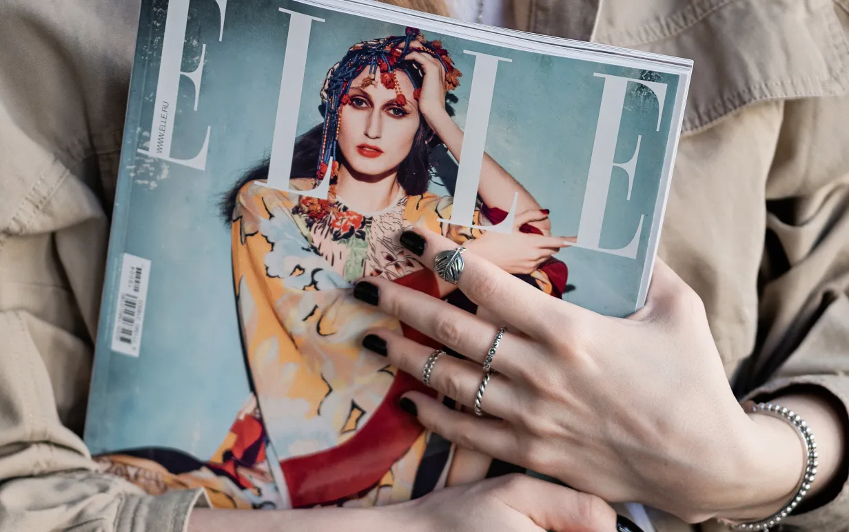 Person iklädd beige jacka håller i ett exemplar av ELLE magazine