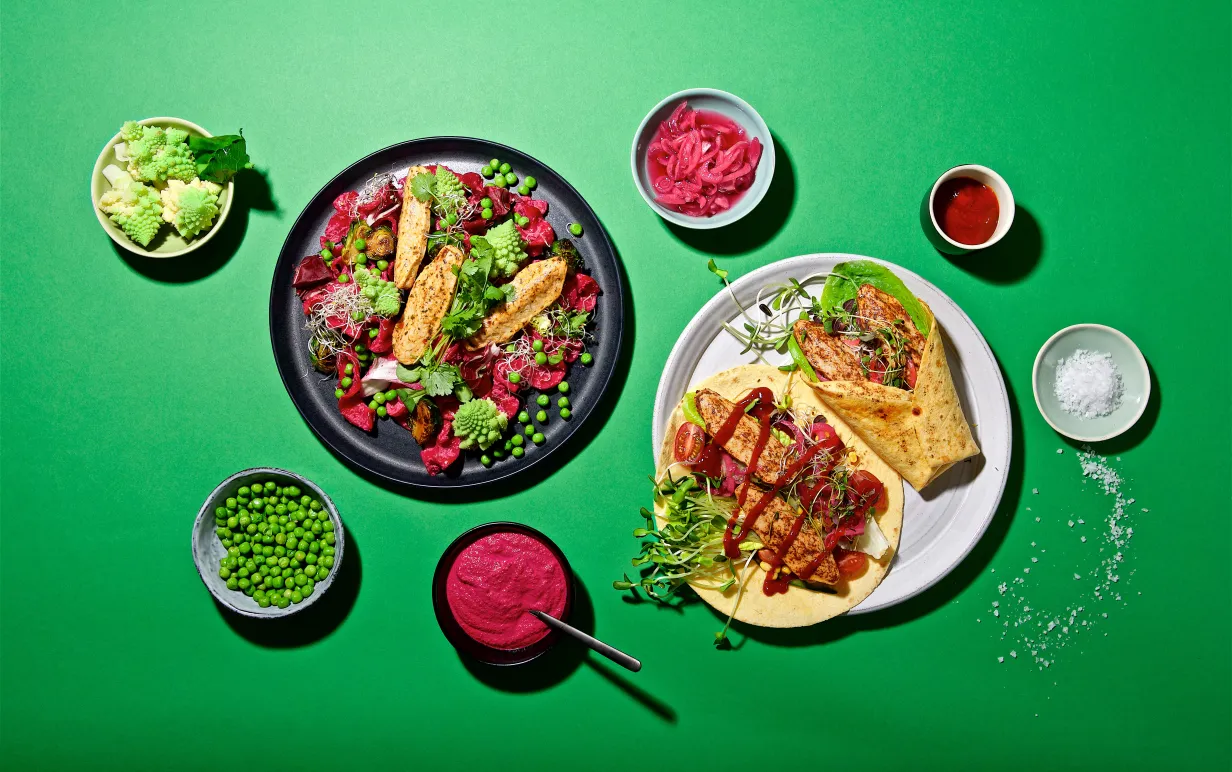 veganska filléer i en sallad på en tallrik och en i wrap på en annan tallrik uppdukat på ett grönt bord med tillbehör.