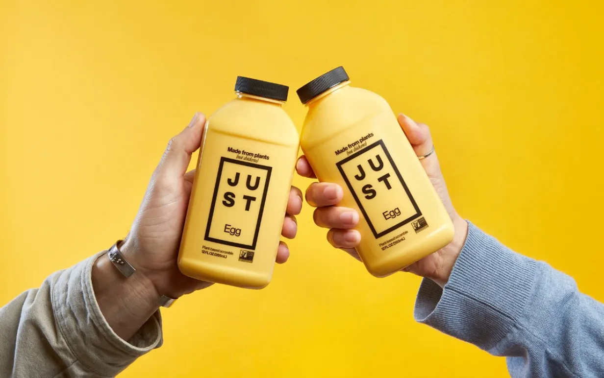 Två händer som håller upp en varsin plastflaska mot varandra mot en gul bakgrund.