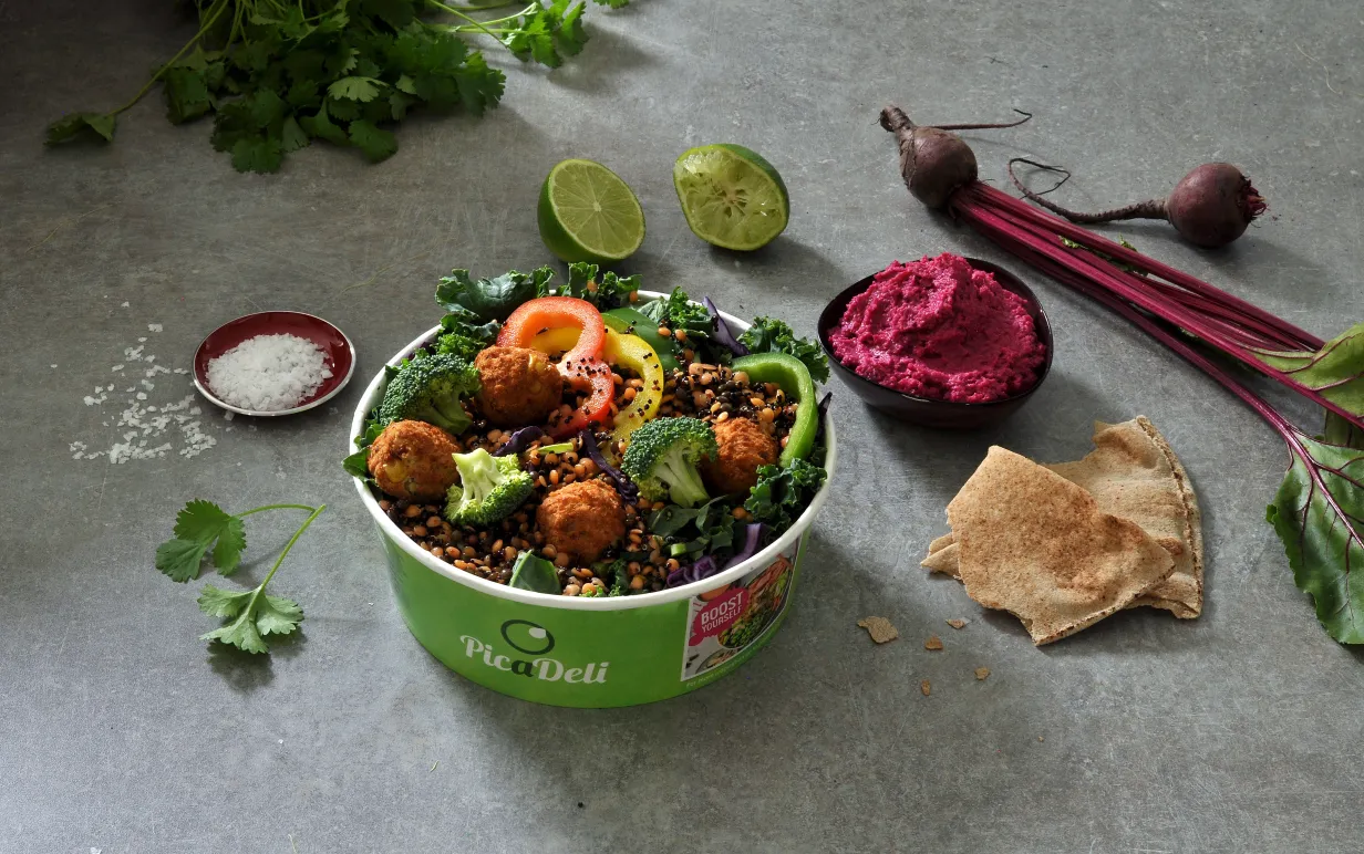 Växtbaserad sallad i en picadelibehållare med olika grönsaker utspridda runt om på ett granitgrått bord.