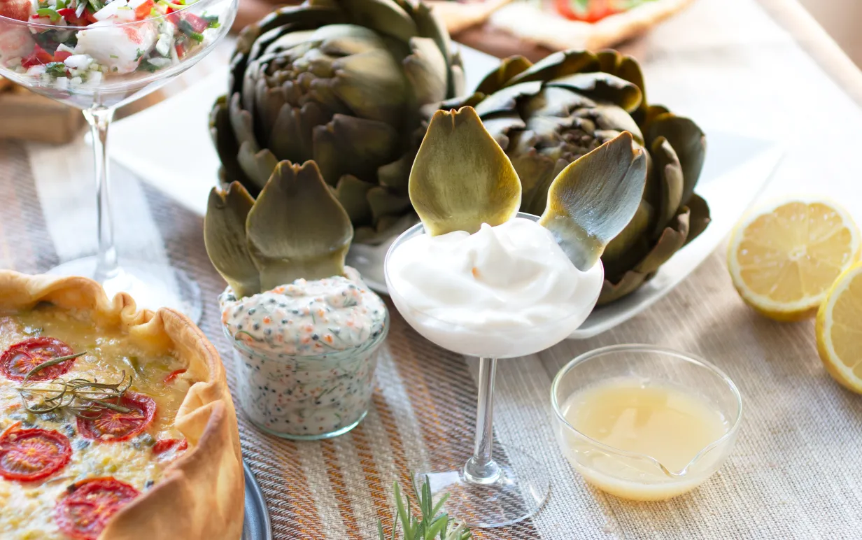 kokad kronärtskocka med tre olika dippar dukade på ett bord bredvid en paj