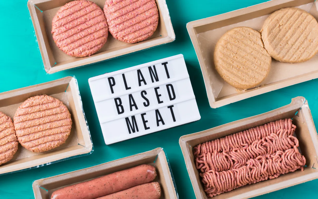 Växtbaserade köttsorrter som burgare, korv och färs, upplagda på ett turkost bord.