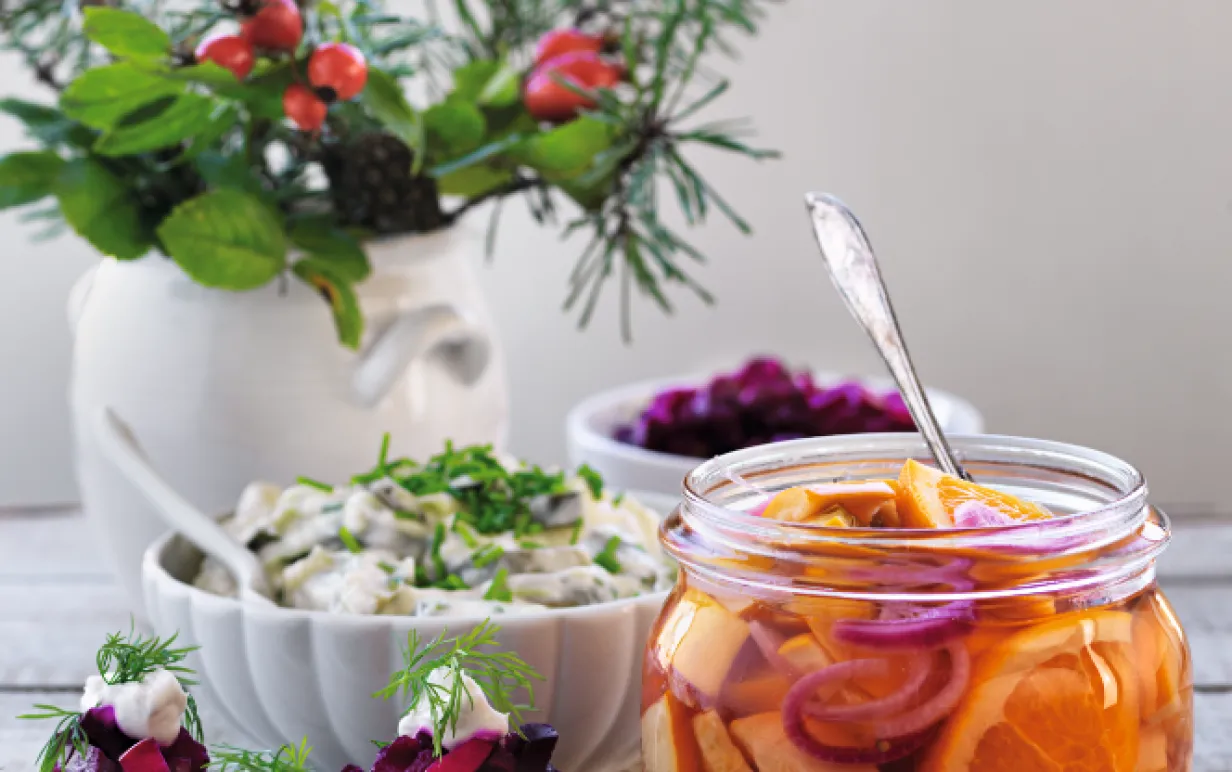 Picklad zucchini med apelsin i en glasburk bredvid snittar och vas med blomster
