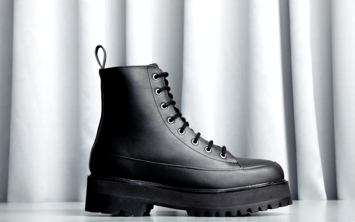 Svart veganska hög känga mot ett ljusgrått draperi