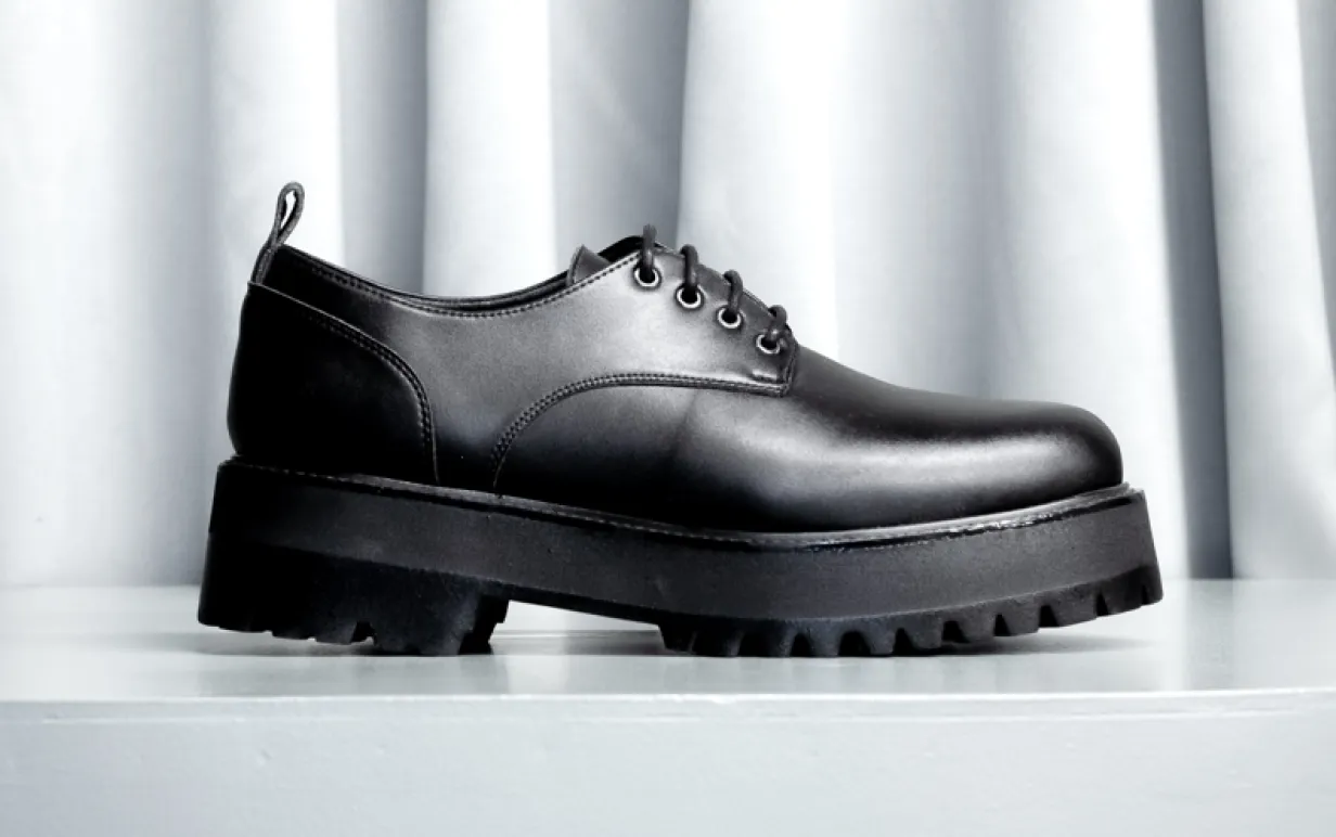 Svart veganska låg känga mot ett ljusgrått draperi