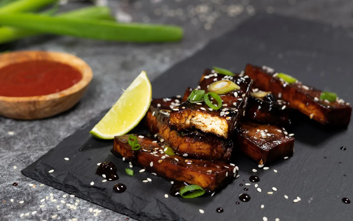 Veganska revbensspjäll av tofu som ligger på ett svart stenblock mot en grå bakgrund