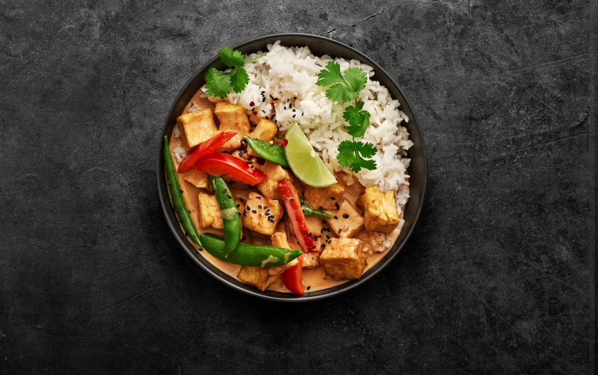 röd currygryta med ris i en djuptallrik vinkel uppifrån mot en granitgrå bakgrund