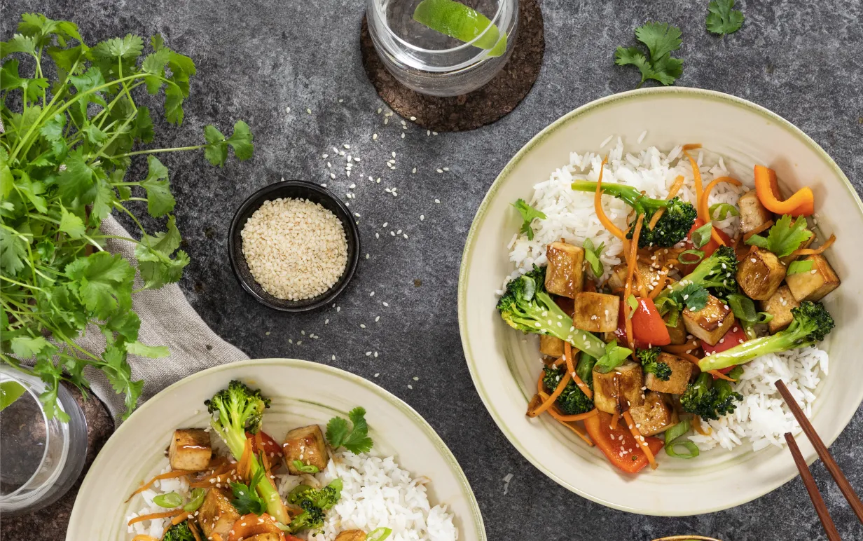 Wok med ros i två tallrikar taget ovanifrån mot ett grått bord