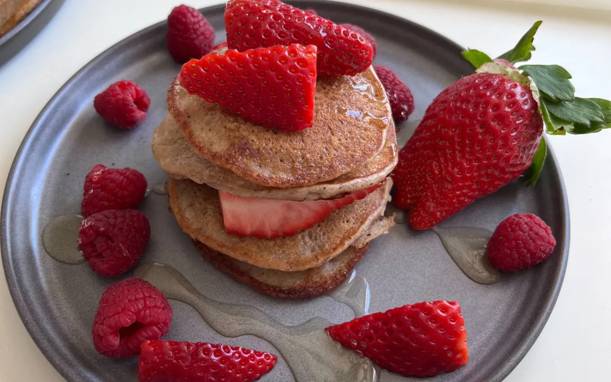 Amerikanska pannkakor staplade på ett grått fat med jordgubbar och hallon
